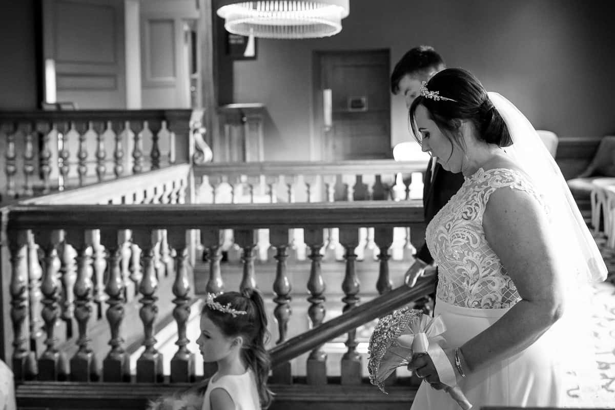 Bride on her way to the ceremony via the beautiful wooden staircase at Abbey House Hotel, Barrow in Furness