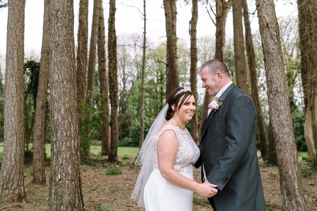 Bride and groom laughing and embracing in the woods on the grounds of Abbey House Hotel on their wedding day