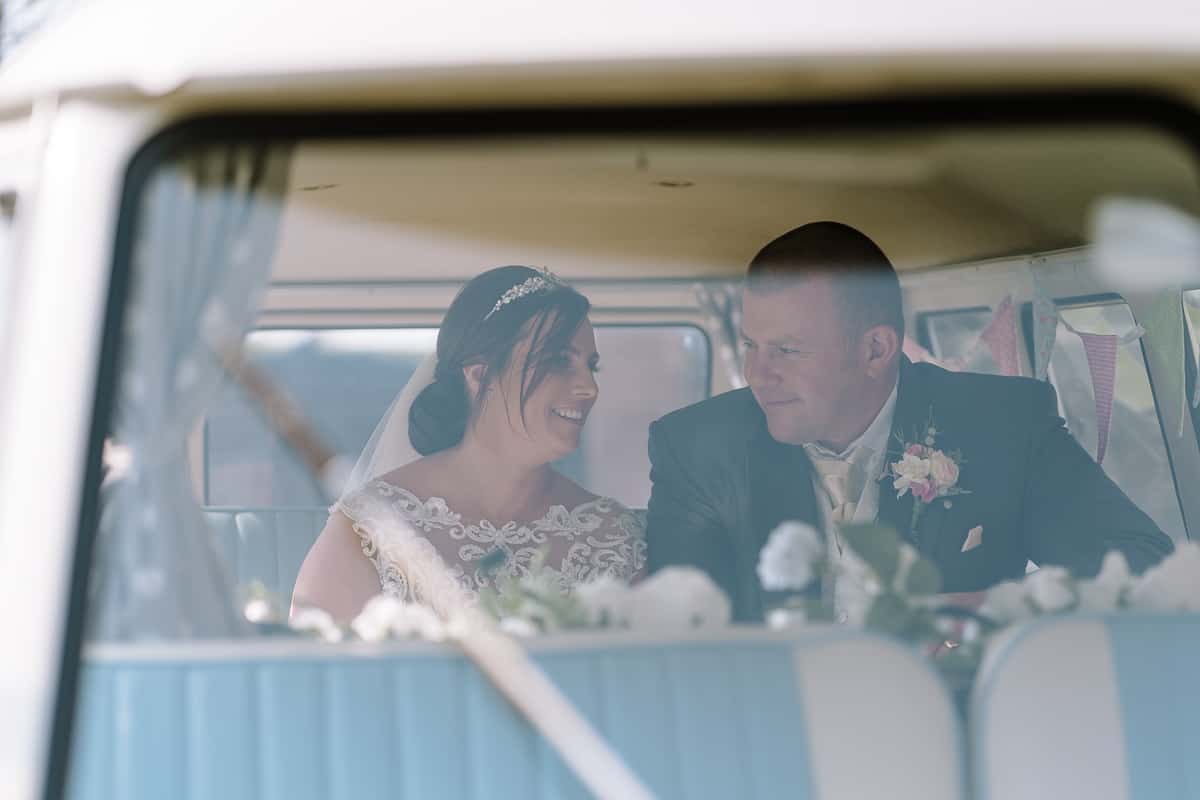 Bride and groom in the VW campervan exchanging smiles on their wedding day