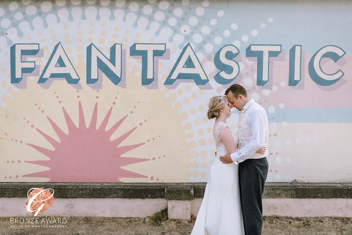 Bride and groom holding each other in front of wall art at the Midland Hotel, Morecambe